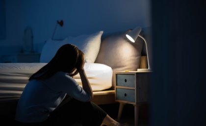 A teenage girl sitting with her head in her hands in a dark bedroom.